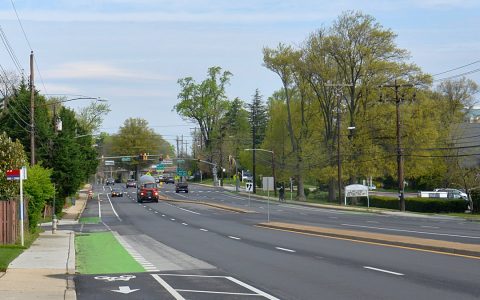 A wide suburban road with green-painted bike lanes approaching a traffic signal