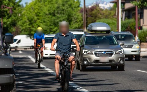 An e-bike rider and a cyclist ride in a bike lane beside traffic