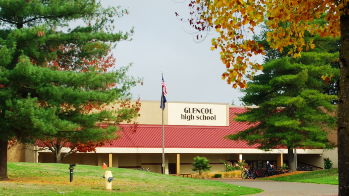 Glencoe High School's entrance framed by pine trees and autumn leaves