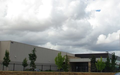 A long, low data center building behind a black fence under a cloudy sky