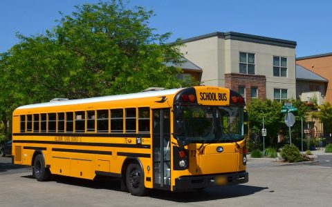 A yellow Hillsboro School District bus turning on a street lined with apartments