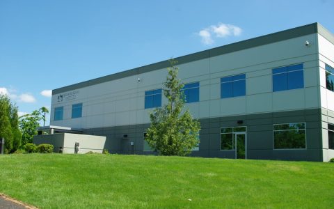 A two-story gray office building behind a sloped lawn