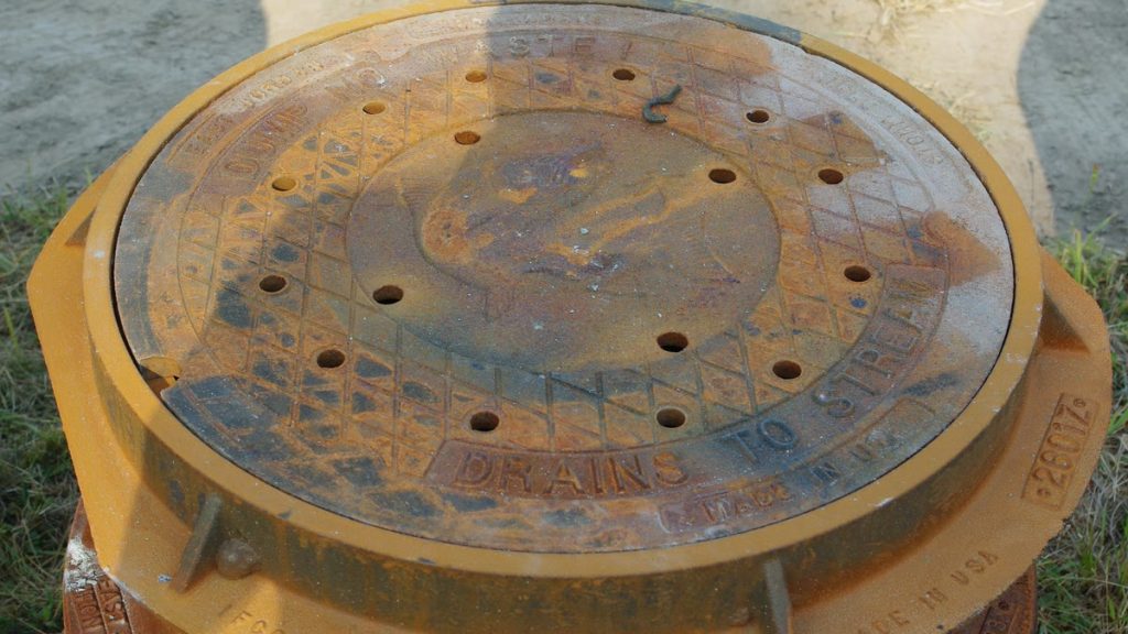 A rusted round storm drain cover stamped Drains to stream