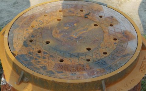 A rusted round storm drain cover stamped Drains to stream