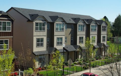 A row of three-story townhomes with small fenced front yards
