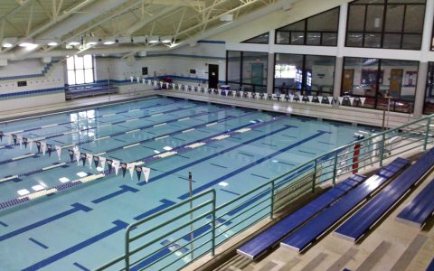 An empty indoor lap pool with lane ropes, flags and spectator benches