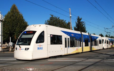 A white MAX light rail train signed for Hillsboro crossing 185th Avenue at street level