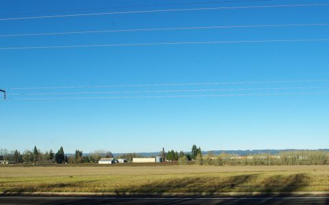 Open farmland under power lines with low buildings and trees in the distance