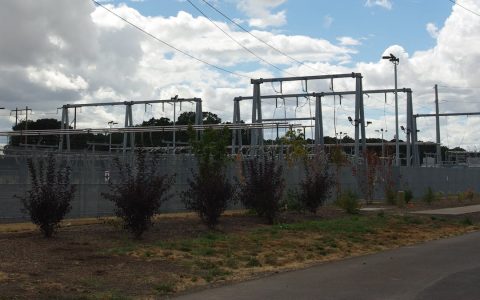 Steel towers of an electrical substation behind a fence and shrubs