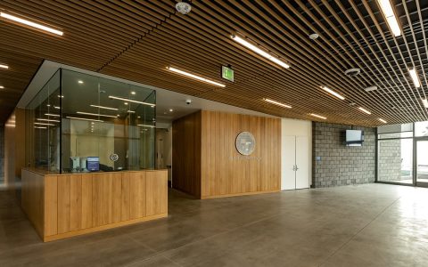 An empty police station lobby with a glass reception window and wood paneling