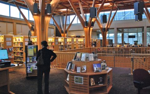 Bookshelves and a display stand under a wooden timber ceiling in a public library