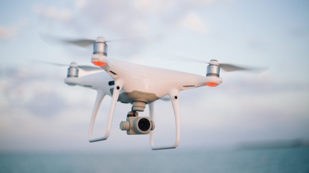 A white quadcopter camera drone in flight against a cloudy sky