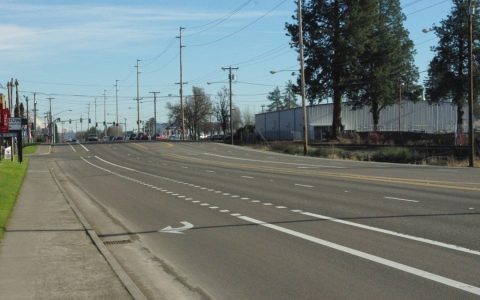 A multi-lane highway with a bike lane and sidewalk under a blue sky