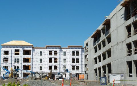 Four-story wood-frame apartment buildings under construction with lifts and fencing